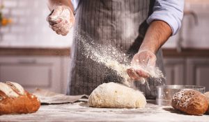 UV decontamination solutions for bakeries and bread production Baker preparing a raw loaf of bread on a table with baked bread and a bun nearby, illustrating UV decontamination of air, surfaces and equipment in bakery operations.